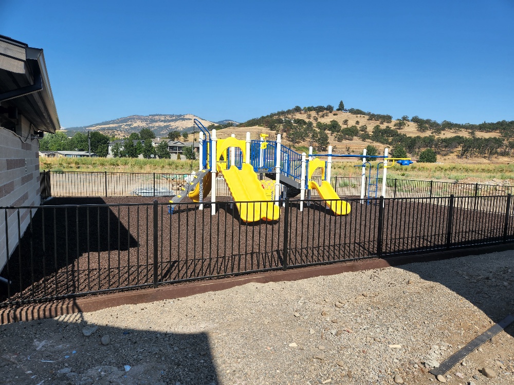A playground with a yellow slide and a fence.