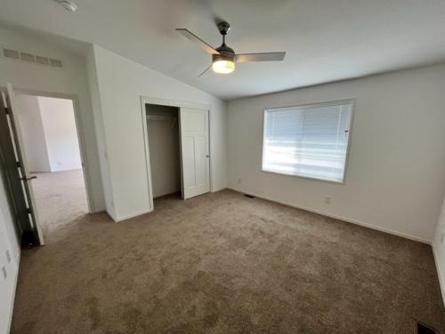 An empty room with tan carpet and a ceiling fan.