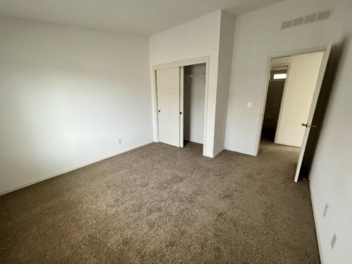 An empty room with tan carpet and closets.
