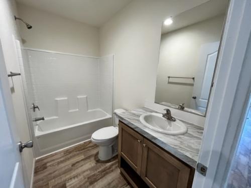 A white bathroom with wood floors and a toilet.