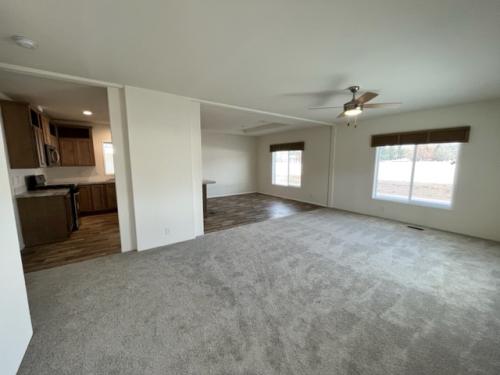 An empty living room with carpet and a ceiling fan.